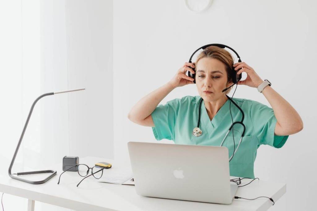 Questions To Ask Yourself and Healthcare Practice - Nurse in Green medical outfit wearing headphones in front of a silver MacBook. 