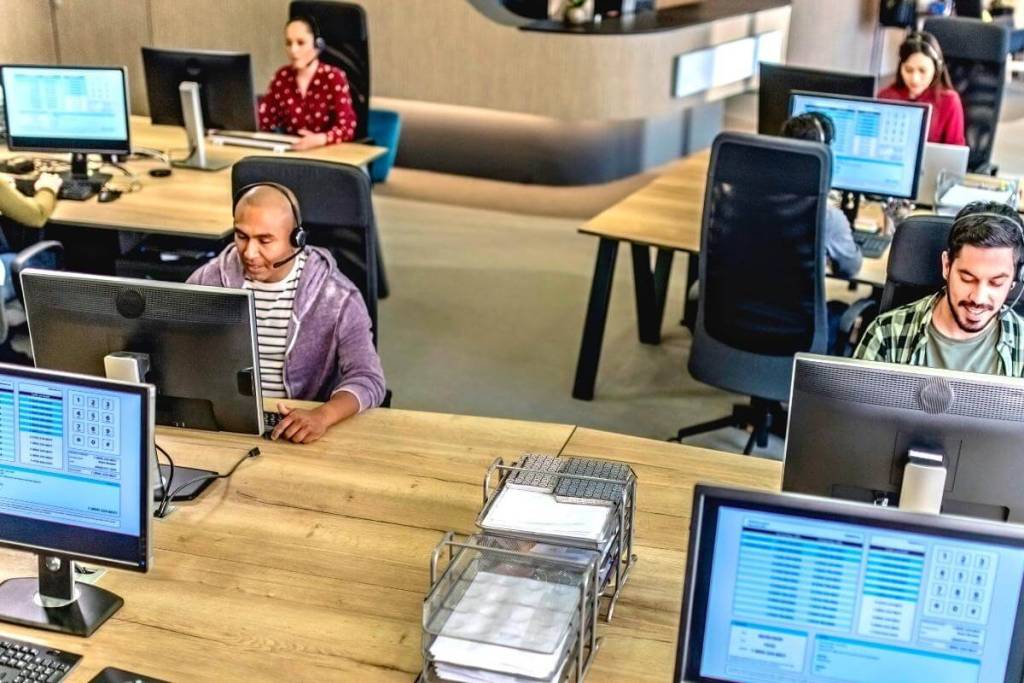 Customer Support Outsourcing - featured image - Cell center employees - group of people sitting behind desks using computers while talking to customers over the phone.