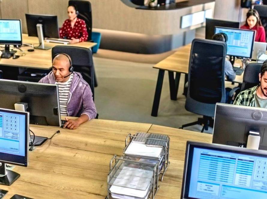 Customer Support Outsourcing - featured image - Cell center employees - group of people sitting behind desks using computers while talking to customers over the phone.