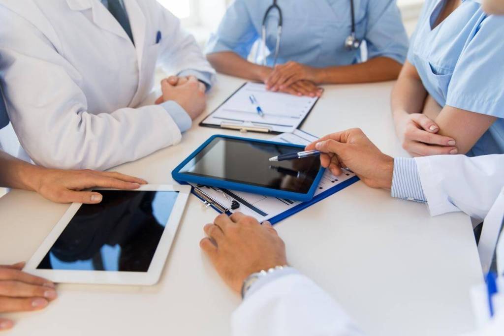 Group of doctors on a discussion holding tablet pc, computers and clipboards.