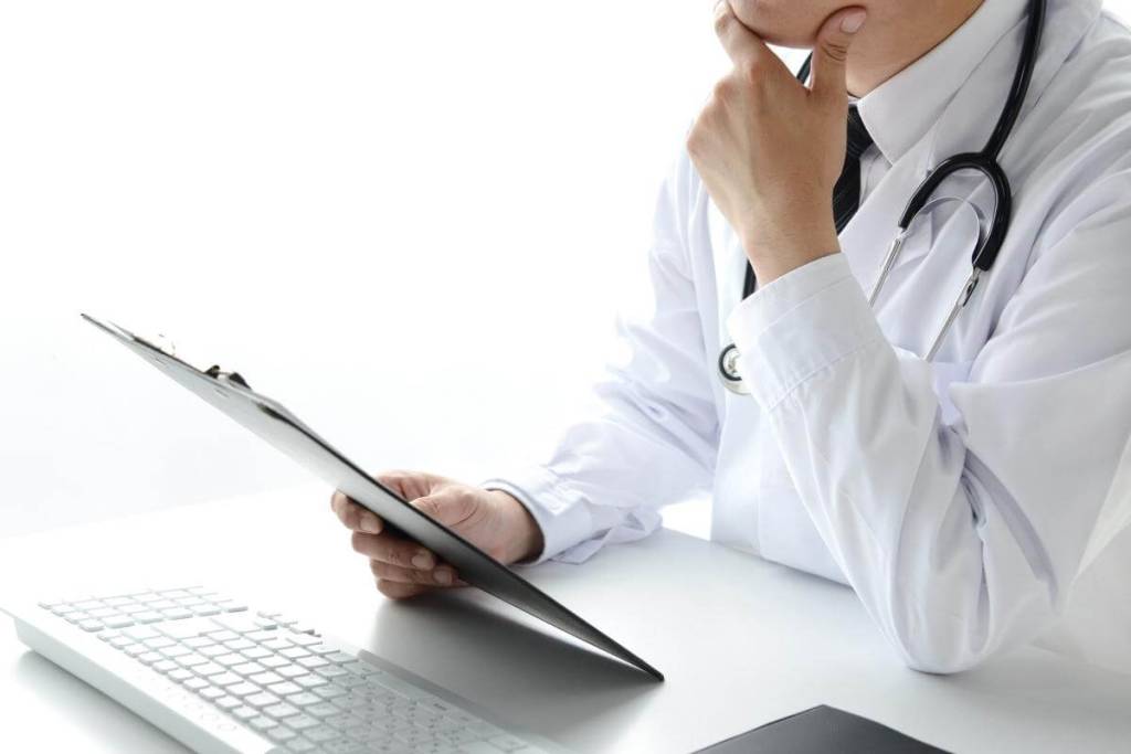 Why Should Dermatology Clinics Consider Outsourced Billing Providers - Doctor thinking holding forms in front of a keyboard. 