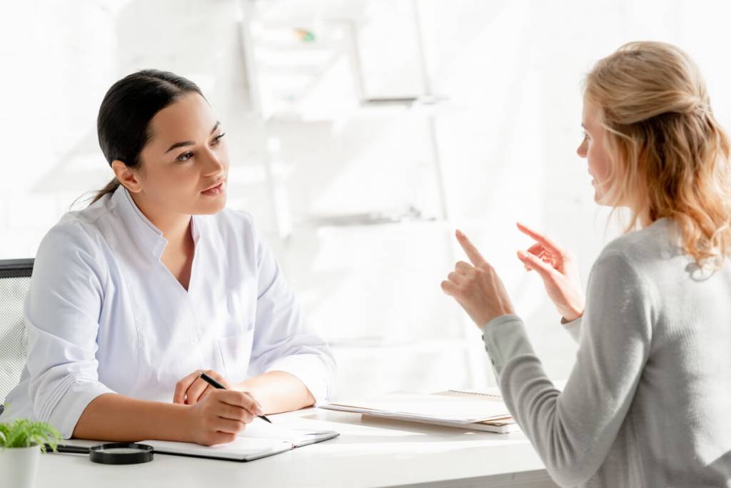 Dermatologist sitting at table and listening to patient in clinic