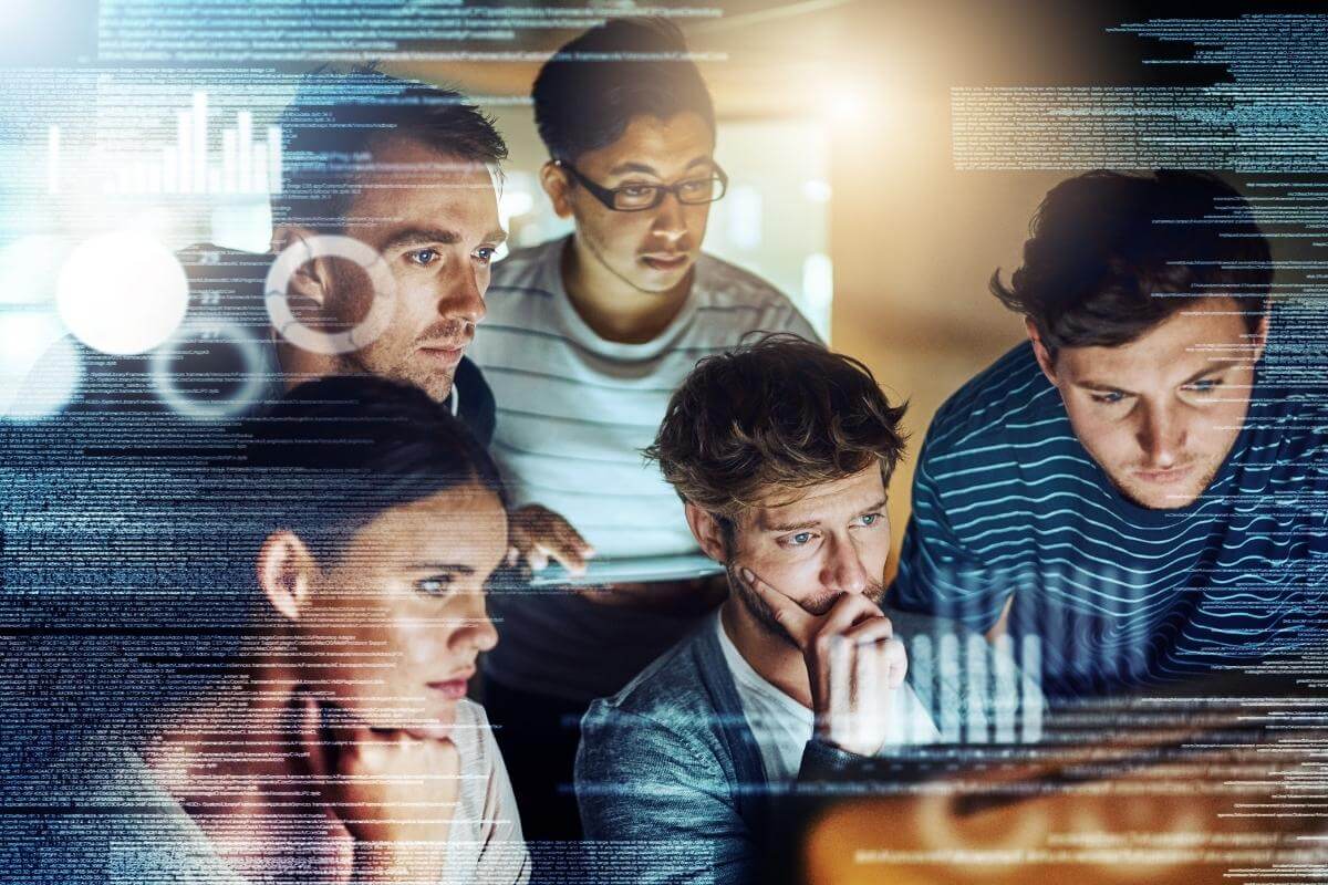 A group of young IT professionals huddle with a virtual screen showing different programming codes