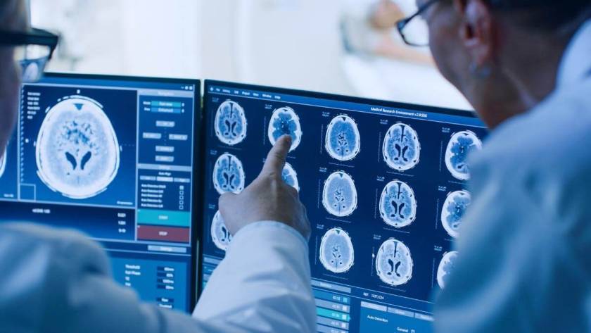Oncology Medical Billing trends - In Control Room Doctor and Radiologist Discuss Diagnosis while Watching Procedure and Monitors Showing Brain Scans Results, In the Background Patient Undergoes MRI or CT Scan Procedure.