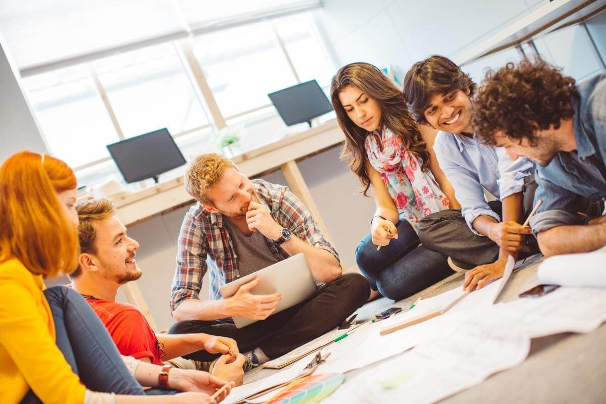 Group of creative people collaborating in an office, sitting on a floor to discusss business project, outsourcing and reports. 