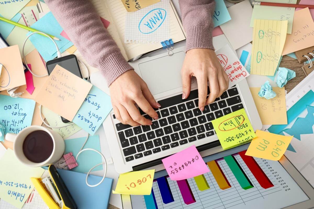 Overwhelmed woman working at messy office desk, top view. 