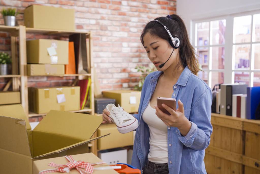 Call Center for E-commerce - Featured Image_Asian businesswoman owner of SME online answer phone call receive from customer on headset checking product shoes before delivery put in cardboxes. Small start up business customer support operator.