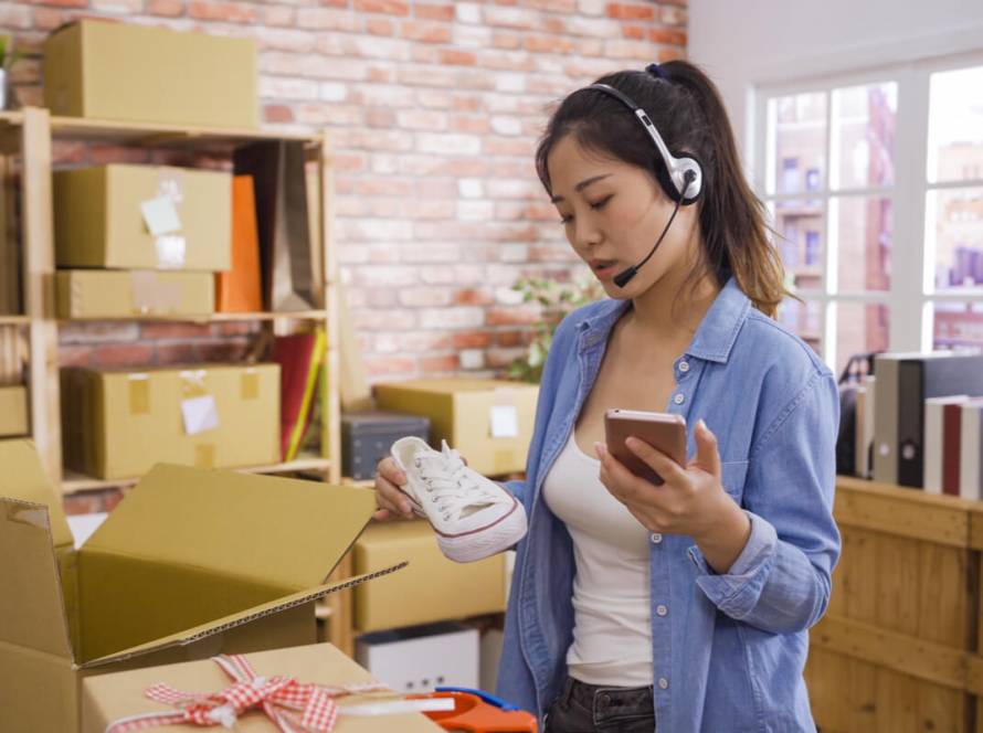 Call Center for E-commerce - Featured Image_Asian businesswoman owner of SME online answer phone call receive from customer on headset checking product shoes before delivery put in cardboxes. Small start up business customer support operator.
