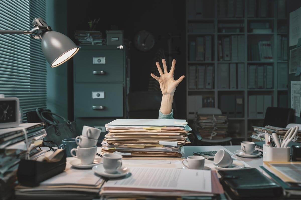 why outsource data entry - Image showing office worker overwhelmed with paperwork asking for help with her hand. 