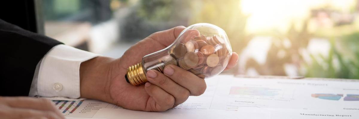 Hand of businessman holding a lightbulb with coins inside. Concept of cost reduction. 