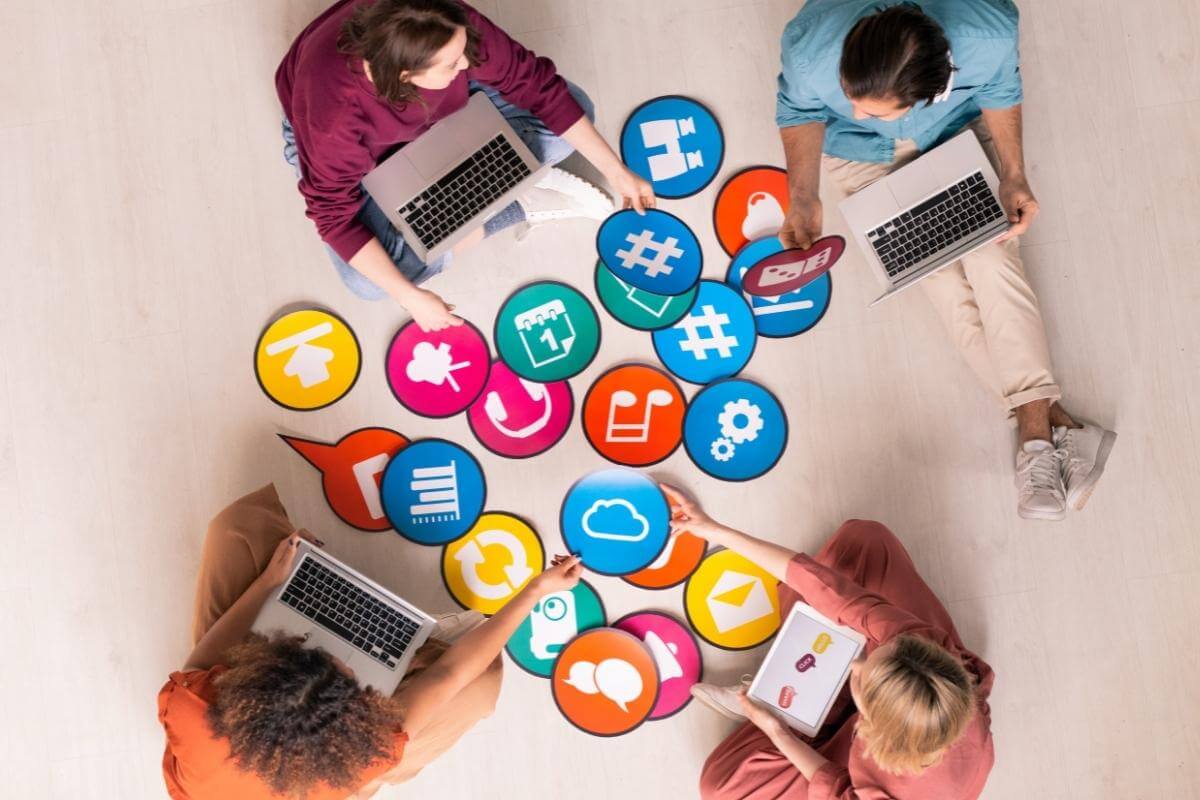 Above view of young social media marketers sitting on a floor and using computers while analyzing reports. 