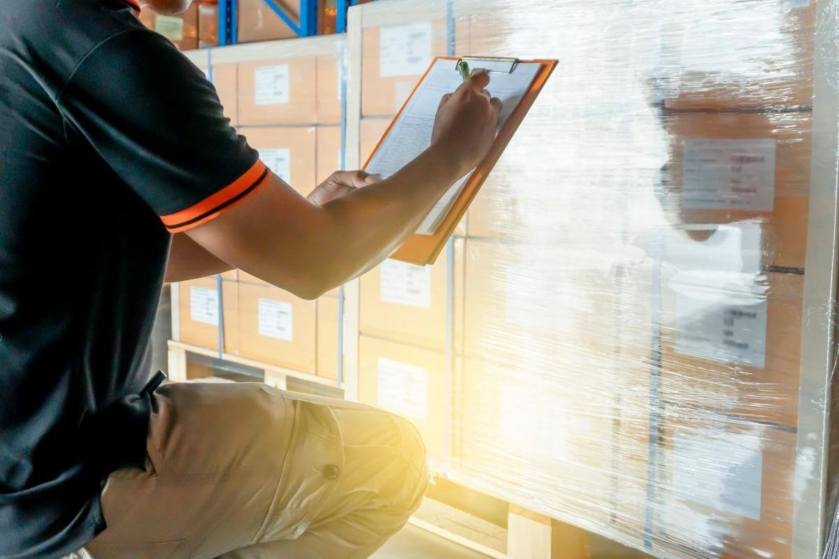 Warehouse inventory management - warehouse worker is writing on a clipboard and inventory stick shipment in distribution. 