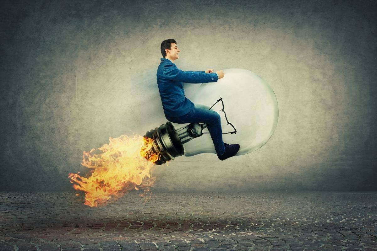 11 Advantages of Customer Support Outsourcing - Young businessman drive on a fast flying light bulb rocket lamp with fire flame on the back. Concept of business success, advantages, benefit and strategy. 