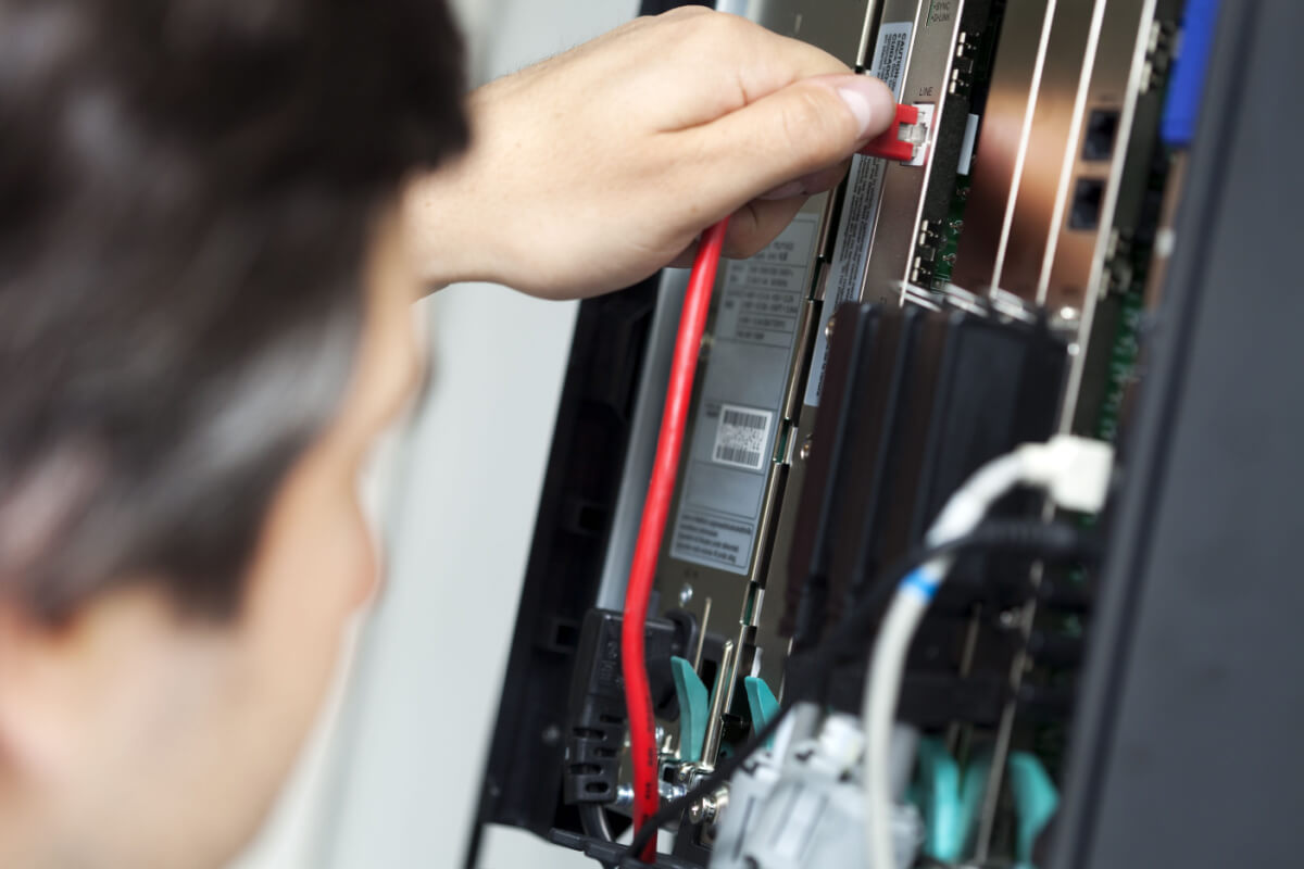 Shallow depth of field close-up of a PBX (private branch exchange), which is a phone exchange for a particular business/office. A technician is plugging in a network cable to the line socket.