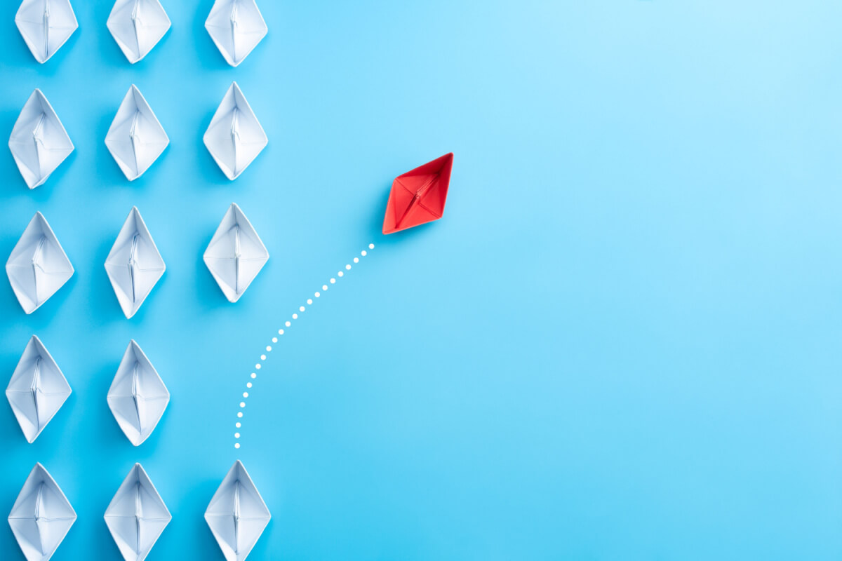 What To Look for in a CCaaS Solution - Group of white paper ship in one direction and one red paper ship pointing in different way on blue background. Business for innovative solution concept.
